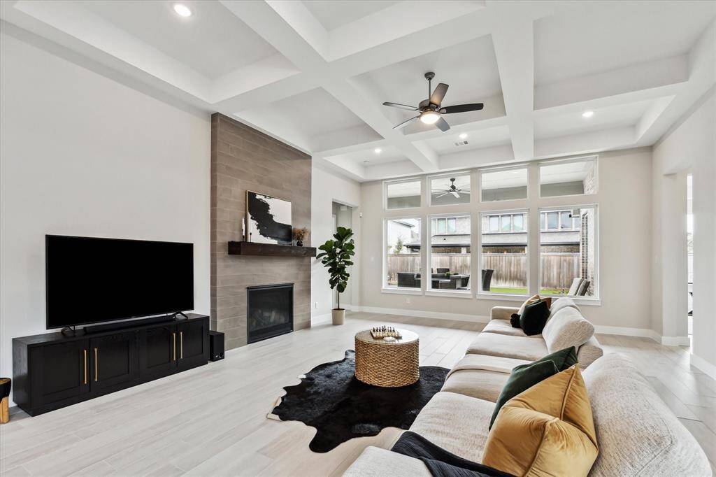 This spacious living room boasts a modern design with a coffered ceiling, large windows for natural light, and a cozy fireplace.
