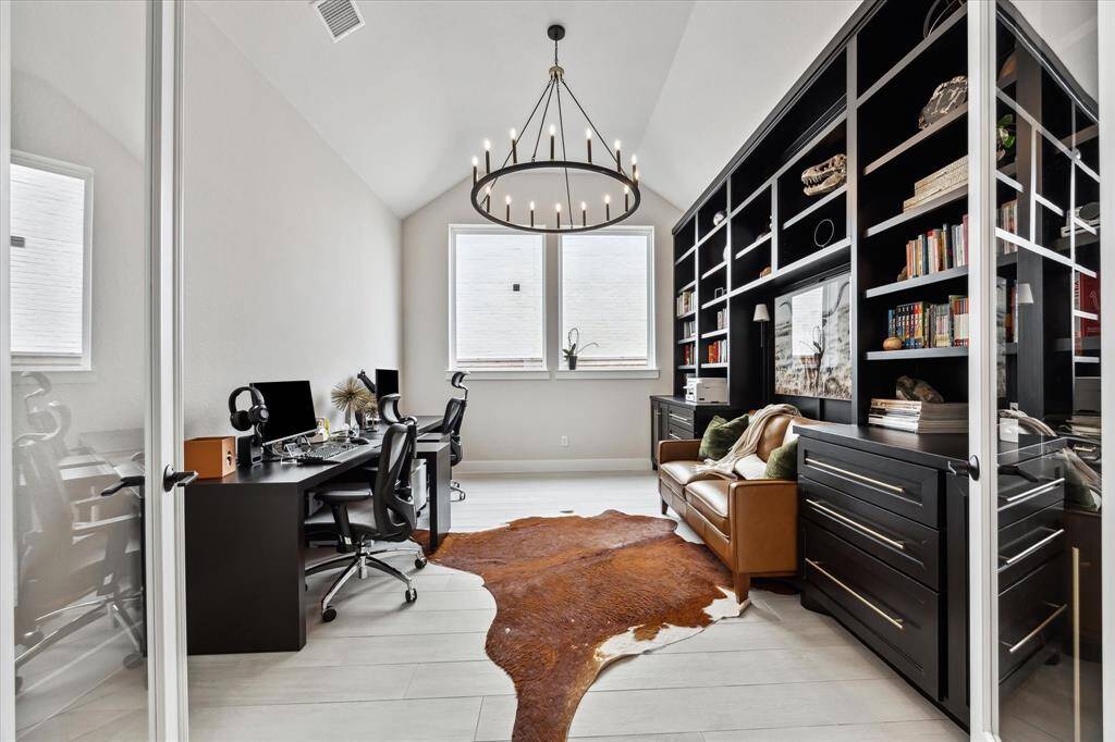 This home office features a modern, sleek design with high ceilings and large windows. It includes a spacious built-in bookshelf, setup perfect for productivity.