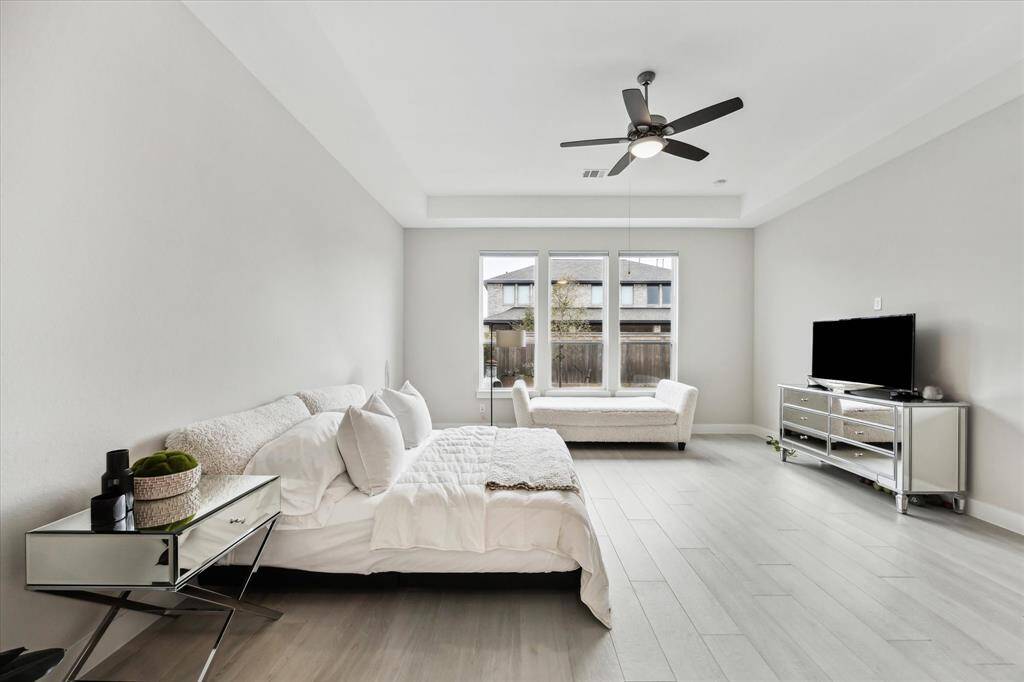 This spacious primary bedroom features a neutral color palette, and ample natural light from large windows.
