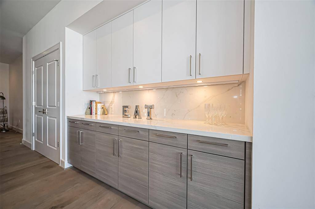 Modern home office features a sleek glass desk, stylish decor with a globe and clock, a large wall mirror, and neutral tones. The space is bright and inviting, perfect for productivity.