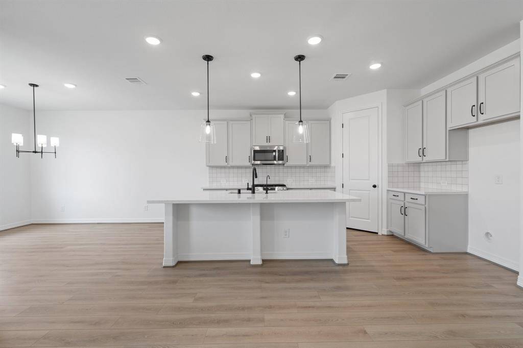 This light and bright kitchen features a large quartz island, white cabinets, a large sink overlooking your family room, recessed lighting, and beautiful backsplash.