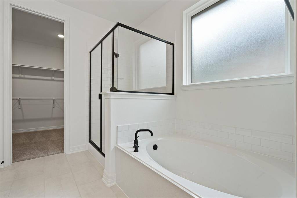 This additional view of your primary bathroom features tile flooring, fresh paint, walk-in shower, a separate garden tub, and a large walk-in closet.