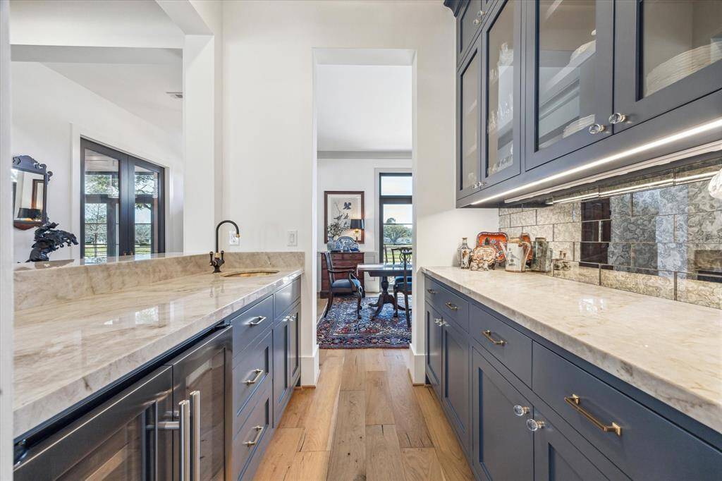 Wet bar doubles as a butler’s pantry with quartzite countertops for serving, smoked mirrored tile backsplash, glass front cabinets for barware and china.  Multiple drawers and cabinets for storage and combination wine/beverage refrigerator.