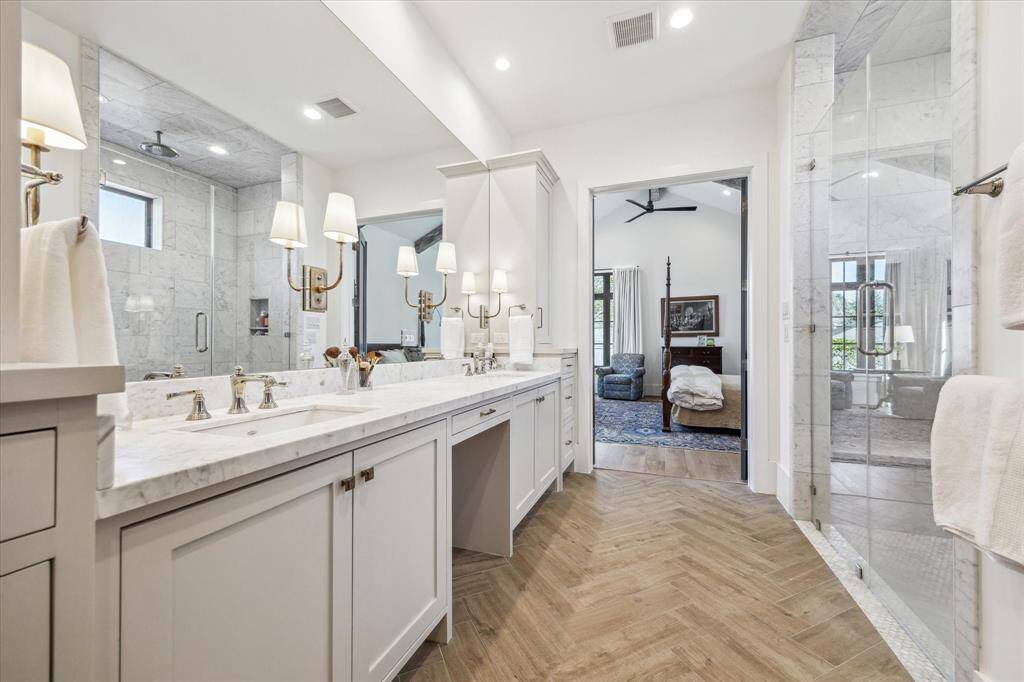 Immaculate marble primary bath with herringbone tile floor, double sink and vanity area.