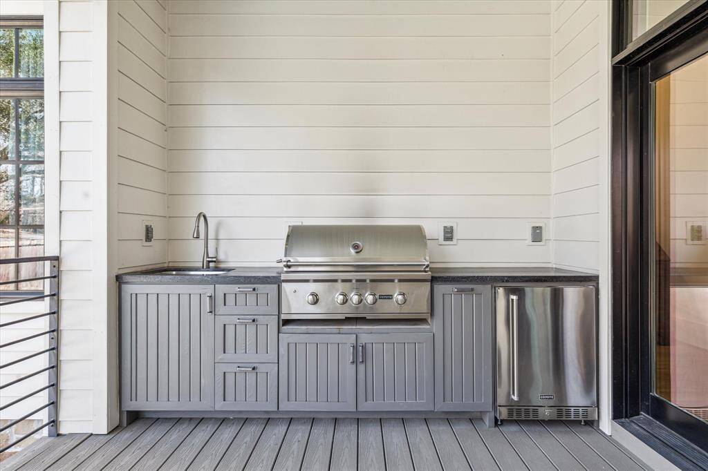 Summer kitchen with granite counter, stainless sink, gas grill, and beverage refrigerator.