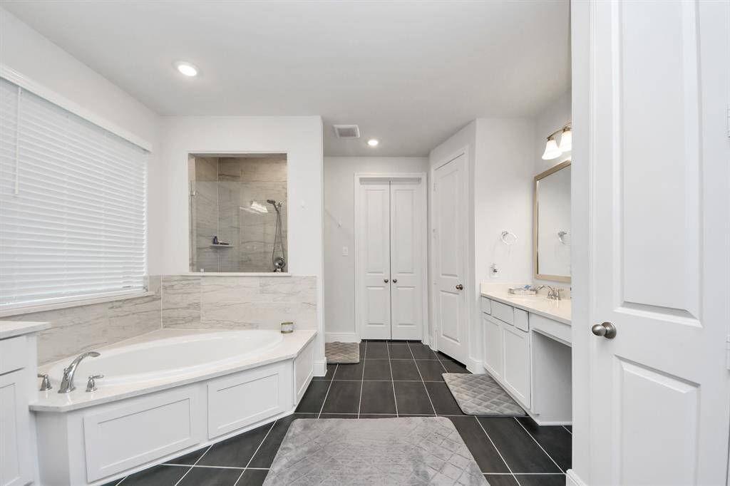 This luxurious en-suite bathroom features his and her sinks, each with its own spacious vanity area for ultimate convenience. The room also boasts a large standing shower and a relaxing soaking tub, creating the perfect space to unwind.