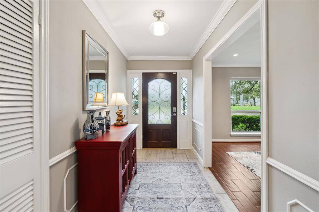 Elegant crown molding, neutral paint tones, and wood-look timeless tile flooring create a warm and refined entrance in this inviting foyer. Abundant natural light streams through the front windows, brightening the space and offering a clear view into the main living area, with the formal dining room to your left for an effortless flow.