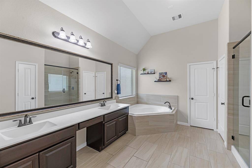 Primary bath with dual vanities, beauty bar, framed mirror, soaking tub, and separate glass shower