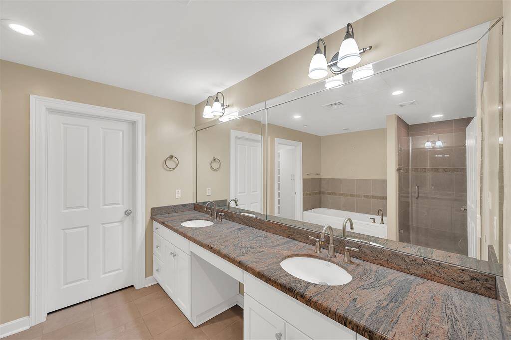 Gorgeous multi color stone countertops of Primary Bath has two undermount sinks with replaced plumbing fixtures. Nice storage in cabinetry with open vanity seating space. You can see the glass enclosure of the shower beside jetted soaking tub in mirror reflection.