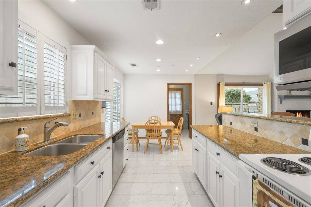 The sleek granite countertops, classic white cabinetry, and elegant tiled backsplash create a timeless aesthetic. Recessed lighting and natural light from large windows brighten the space, while plantation shutters offer charm and privacy.