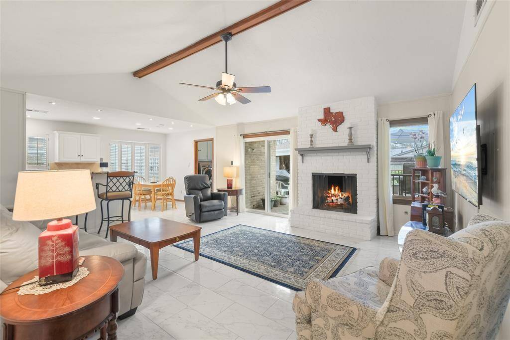 Step into this inviting open-concept living space, where comfort meets style. The vaulted ceiling with exposed wood beam enhances the spaciousness, while the cozy brick fireplace serves as the perfect focal point for relaxing evenings.