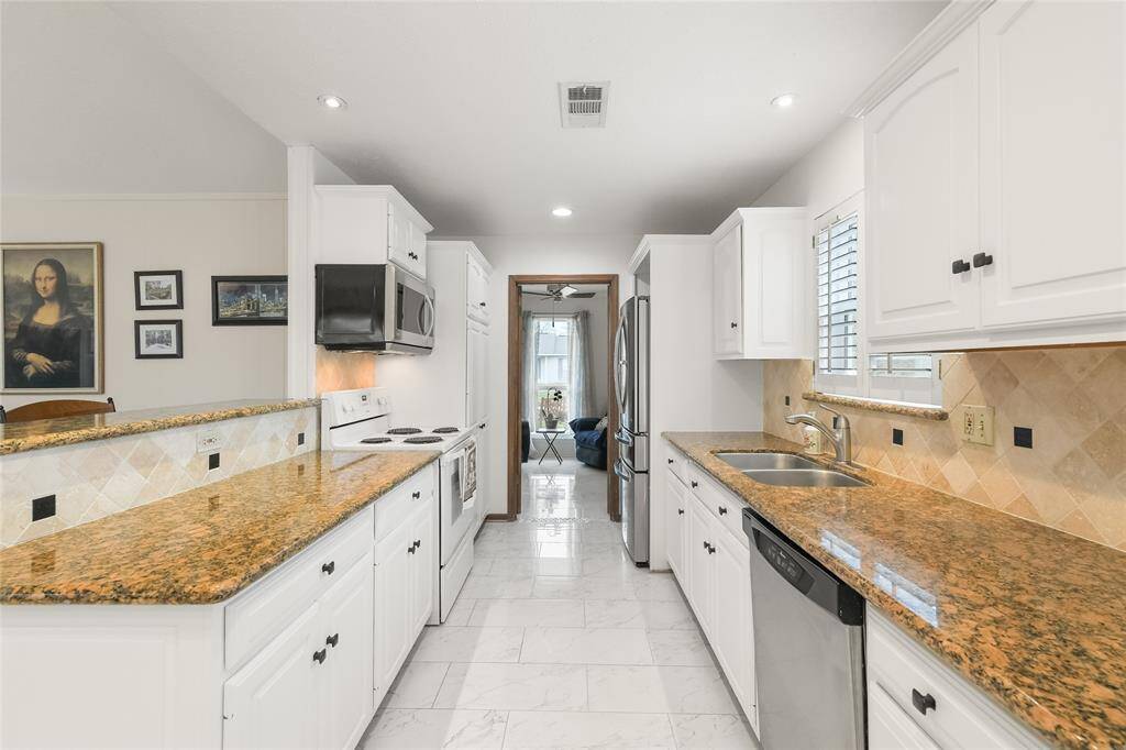This beautifully designed galley-style kitchen is both elegant and efficient, featuring stunning granite countertops that provide ample prep space. The crisp white cabinetry with black hardware creates a timeless contrast, while the tiled backsplash with accent details adds warmth and sophistication.