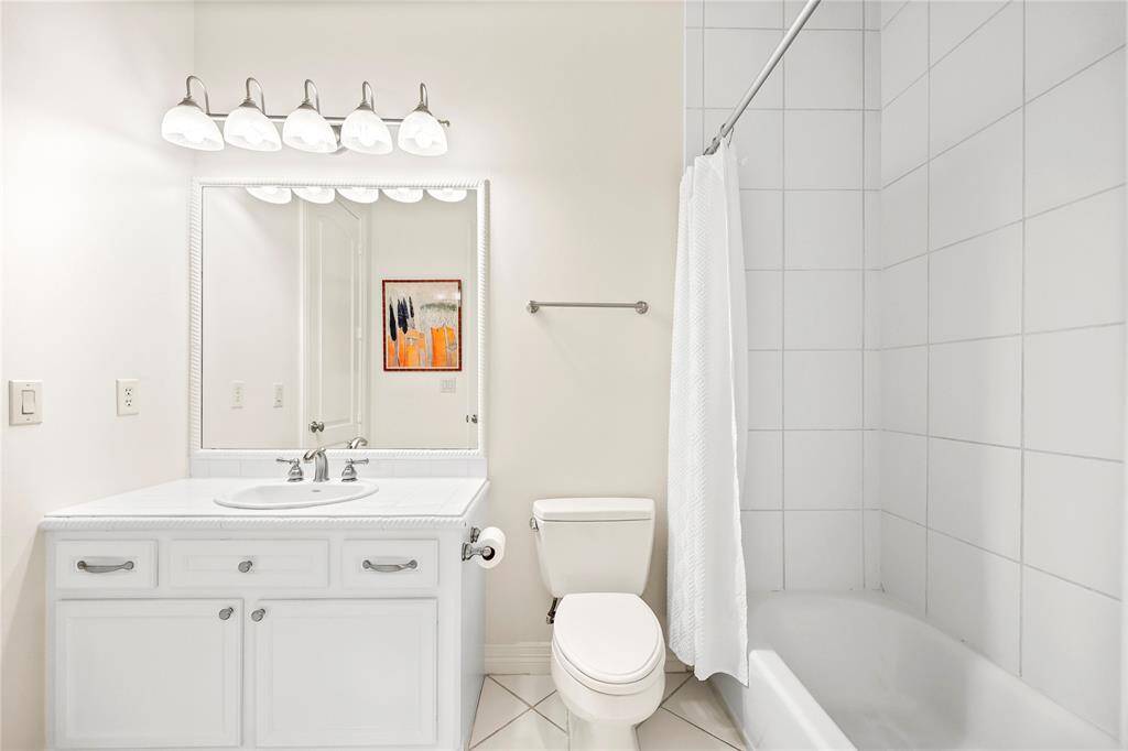 This ensuite bath features a spacious vanity with a tile countertop, overhead vanity lighting, and ample cabinet storage. The room is completed with a tub/shower combo and a walk-in closet for added convenience