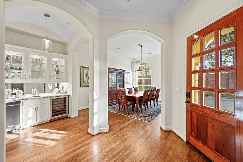 An arched entry from the foyer leads into the elegant formal dining room, featuring two grand radius windows with custom treatments that fill the space with natural light and offer views of the landscaped front yard. built-in ceiling speakers enhance the dining experience, while the room seamlessly connects to the wet bar and wine grotto, making it perfect for entertaining