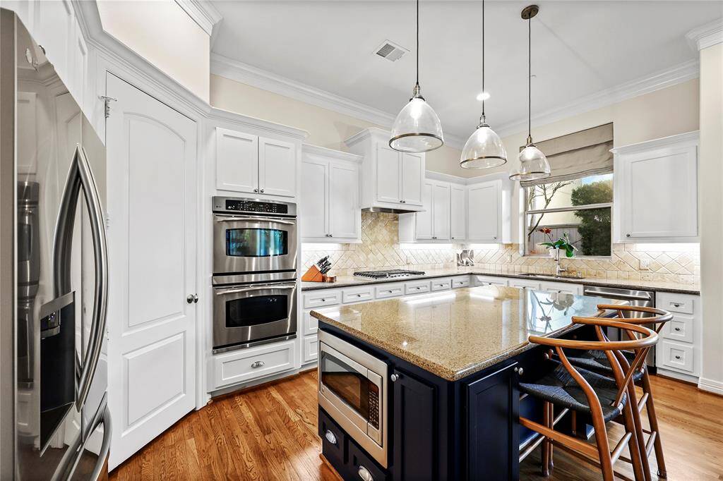 Light and bright cabinetry is complimented by granite countertops and a travertine backsplash, while high-end stainless steel appliances, including a gas cooktop, enhance the cooking experience