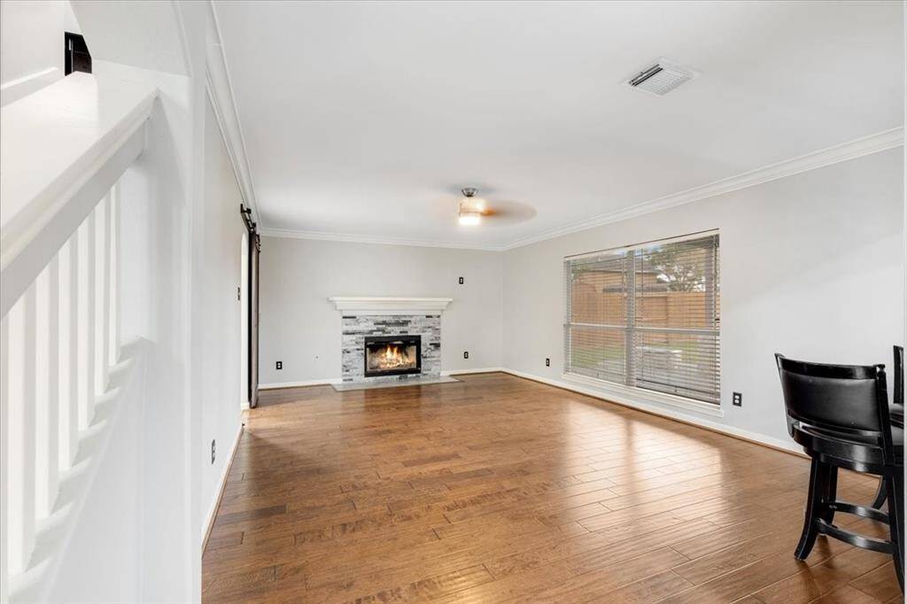 This spacious living room features hardwood flooring, a cozy fireplace with a modern stone surround, and large windows for natural light. The neutral walls and ceiling fan add a contemporary touch.