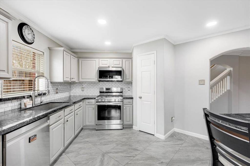 This kitchen features modern appliances, white cabinetry, and a sleek black countertop. The space is bright with ample natural light and has a clean, contemporary design with tile flooring and a classic backsplash.
