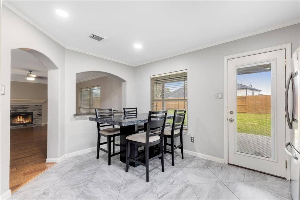 This photo showcases a bright dining area with large windows and a door leading to a fenced backyard. It features a cozy dining set and tiled flooring. An arched opening connects to a living room with a fireplace and wood flooring, enhancing the home's inviting atmosphere.