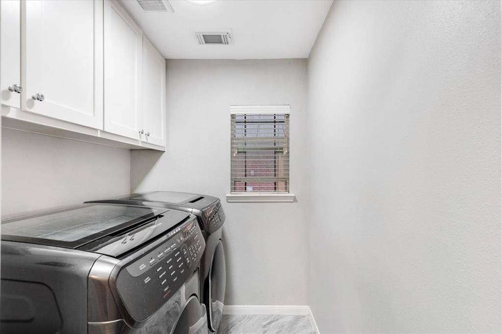 Compact laundry room with modern washer and dryer, white cabinetry for storage, and a small window for natural light.