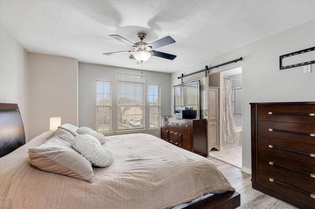 This bedroom features a cozy, well-lit space with a large bed, ceiling fan, and ample natural light from multiple windows.