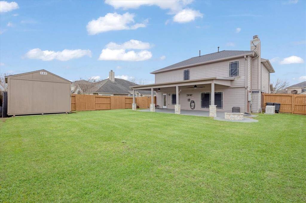 Spacious backyard with well-maintained lawn, featuring a two-story house with a covered patio and a separate storage shed. Ideal for outdoor activities and entertaining.