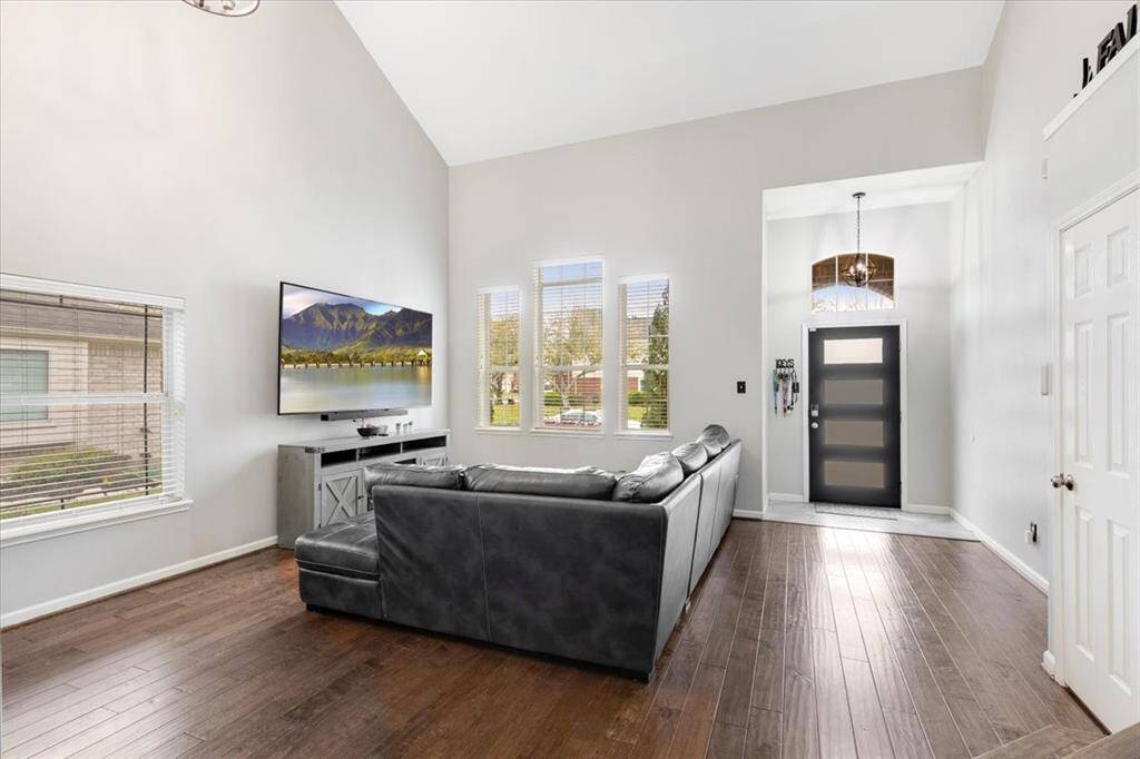 This photo showcases a bright, open living area with high ceilings and hardwood floors. It features a modern, welcoming entryway with a stylish front door and chandelier.