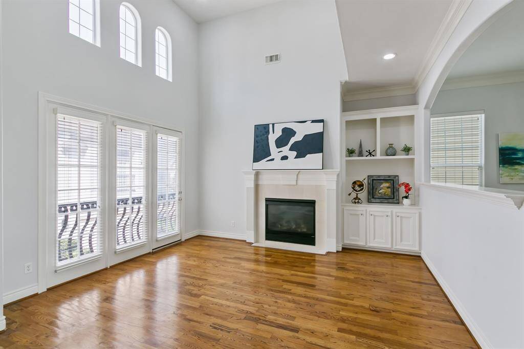 Spacious family room with soaring ceiling, hardwood floors, wall of windows with door to balcony and fireplace with mantel and great shelves with cabinets.