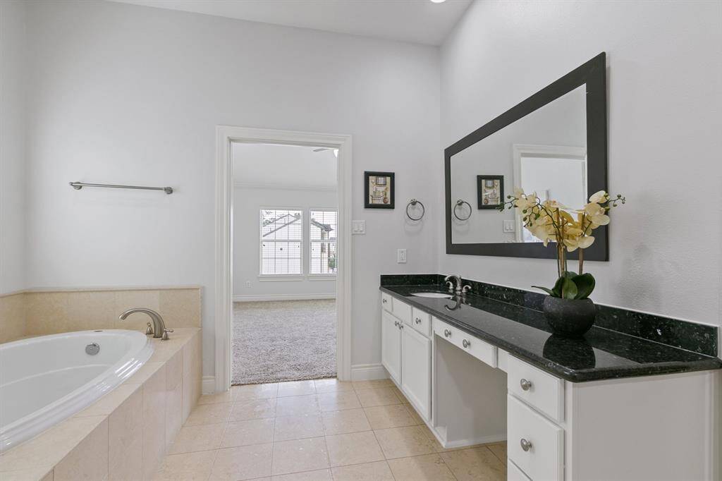 View of freshly painted primary bathroom with tile floor, two vanities each with a sink, and garden tub looking to the owner's suite.