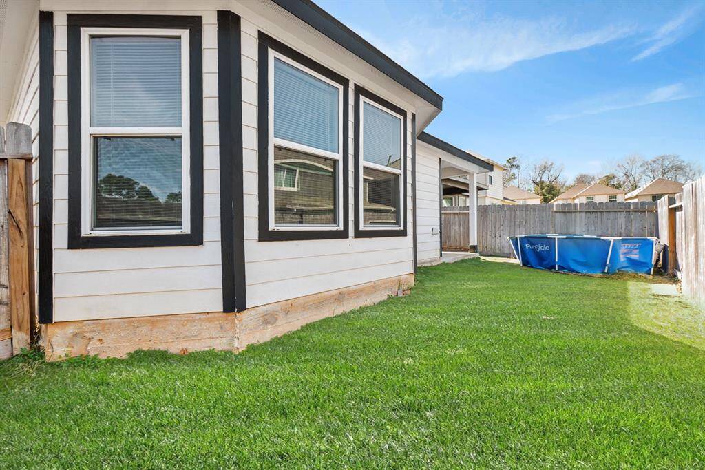 This photo shows a corner of a house with white siding and black trim, featuring large windows. It has a fenced backyard with a small lawn and an above-ground pool, providing a cozy outdoor space.