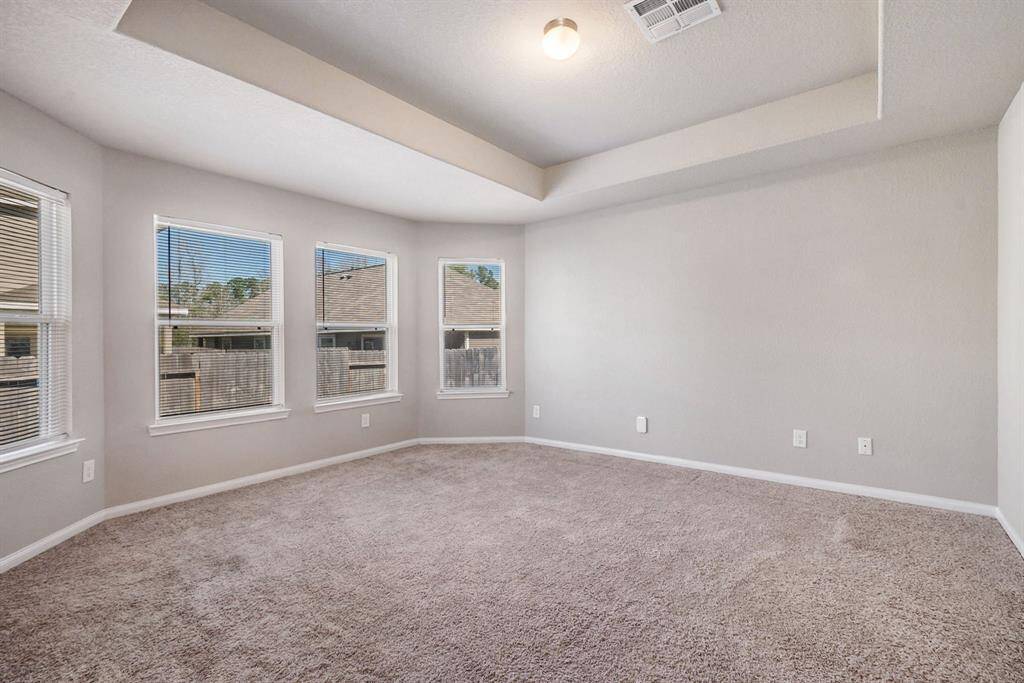 Spacious primary bedroom room with neutral walls and multiple windows, offering plenty of natural light. The ceiling features a decorative tray design, adding architectural interest.