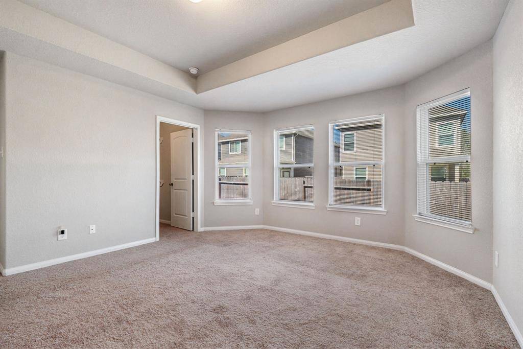 Spacious primary bedroom room with neutral walls and multiple windows, offering plenty of natural light. The ceiling features a decorative tray design, adding architectural interest.