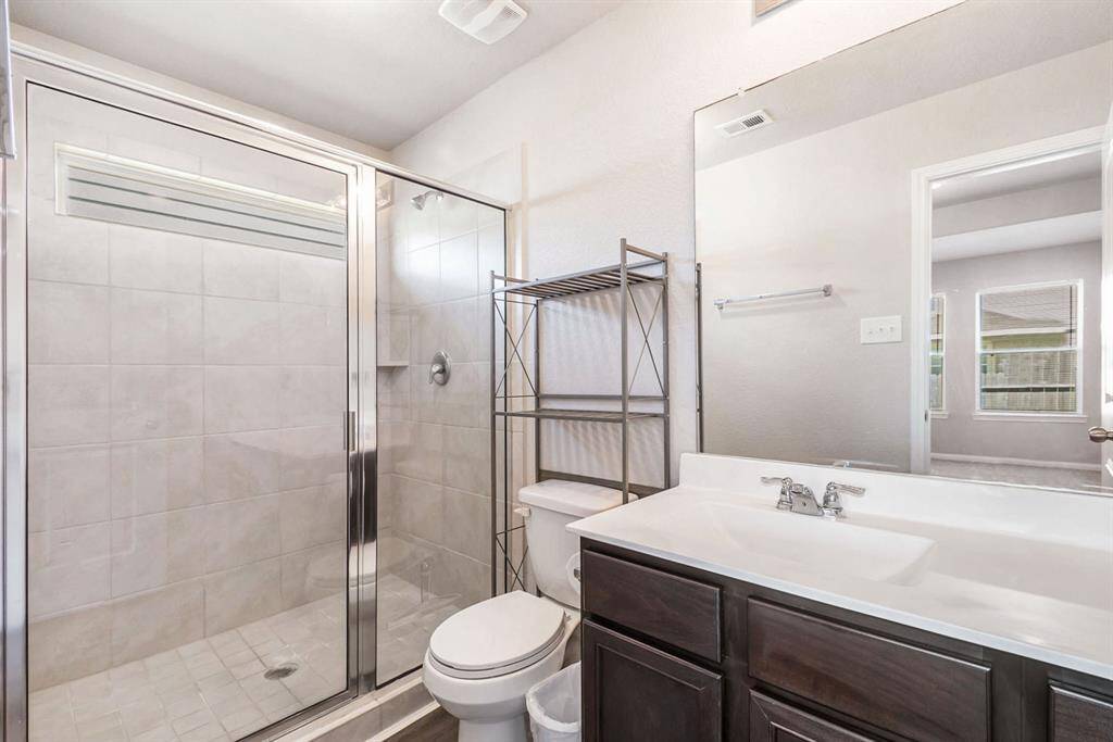 The primary  bathroom features a spacious glass-enclosed shower with tiled walls, a dark wood vanity with a white countertop, and a sleek mirror. Natural light filters in, creating a bright and inviting space.