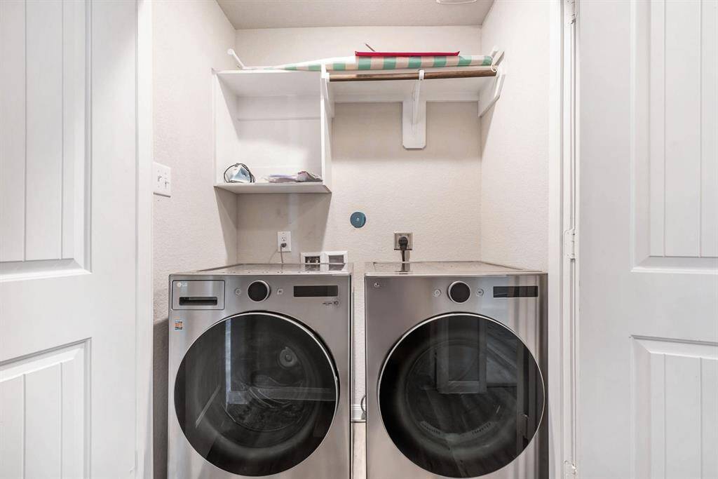 A laundry nook with modern front-loading washer and dryer units. Above them, there's a shelf for storage, ideal for detergents and laundry supplies. The space is well-lit and efficiently organized.
