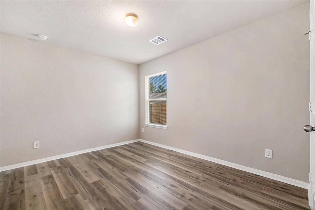 Bedroom two with neutral-color walls and wood flooring. It features a single window allowing natural light and has a modern ceiling light fixture. Ideal for a bedroom or home office.