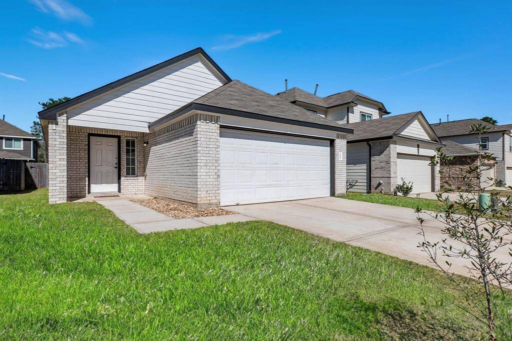 A modern single-story home with a brick exterior and a two-car garage. The driveway and entry path are concrete, surrounded by a well-maintained lawn. The house features a covered entryway, adding charm and functionality.