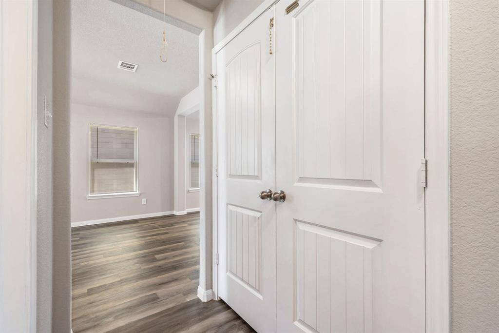 A bright, inviting hallway entry to bedrooms with wood-style flooring and with laundry behind double doors, connecting to living room with large windows.