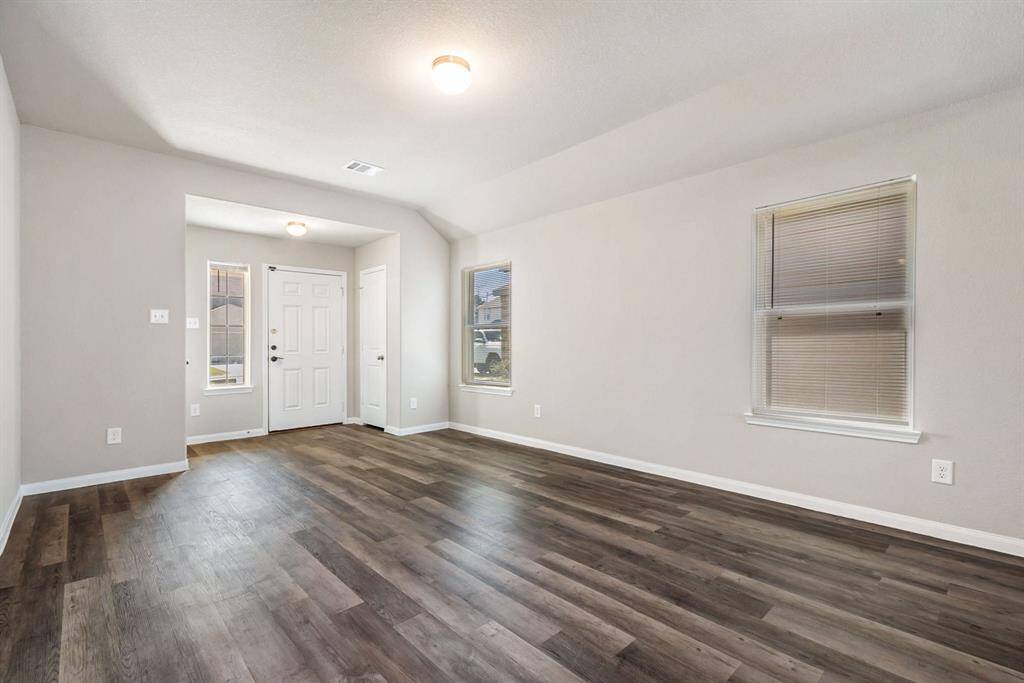 Bright and spacious entryway with wood-look flooring, neutral walls, and ample natural light from the windows. The main entrance door is centered, and the area has a modern, open feel.
