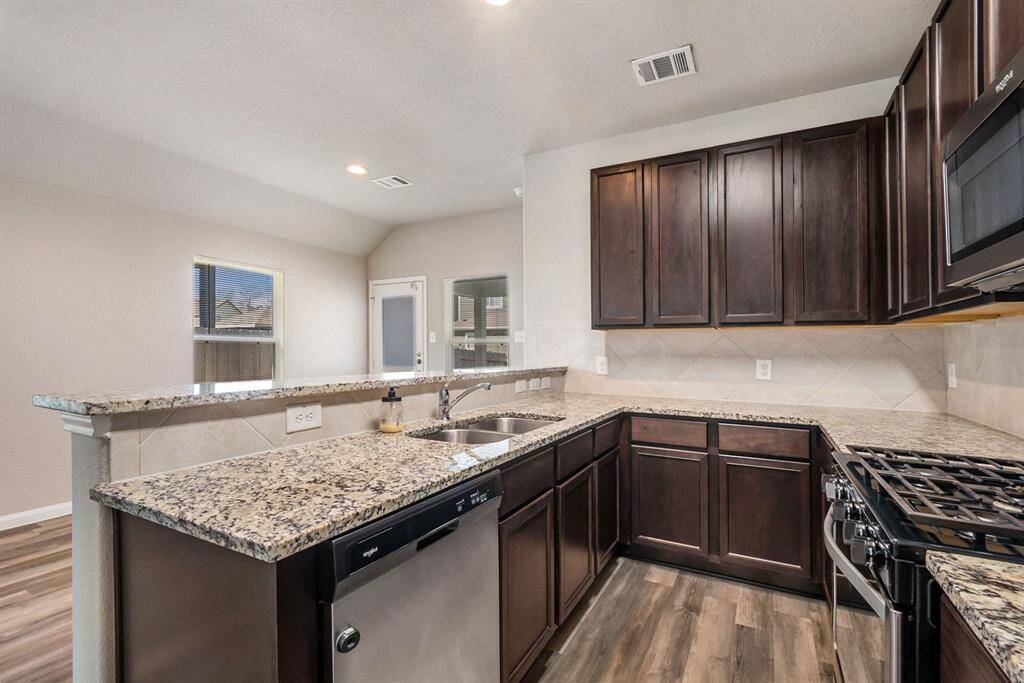 Modern kitchen features dark wood cabinets, granite countertops, and stainless steel appliances. It has an open layout with ample natural light, making it both functional and inviting.