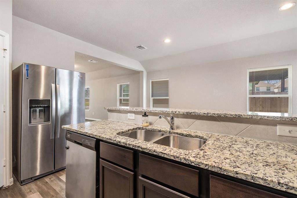 Kitchen features granite countertops, stainless steel appliances, and a double sink. It has an open layout with ample natural light from multiple windows and recessed lighting.
