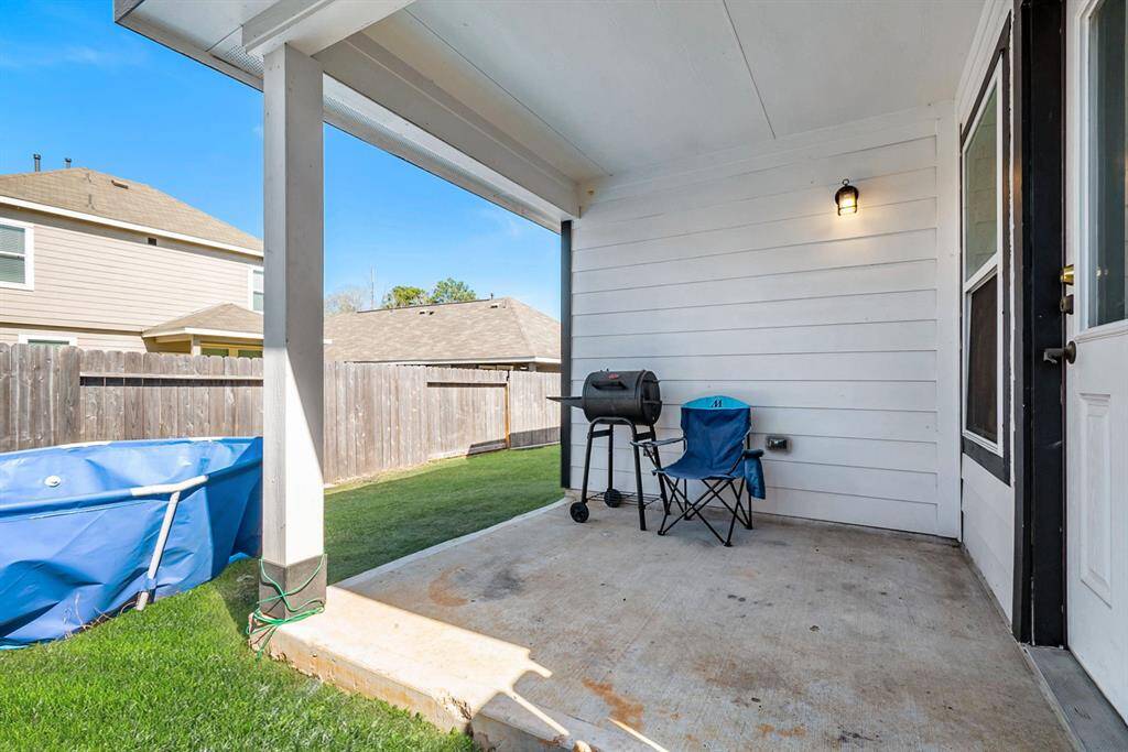 A cozy covered  backyard patio  adjacent to a grassy area enclosed by a wooden fence. Ideal for outdoor relaxation and barbecues.