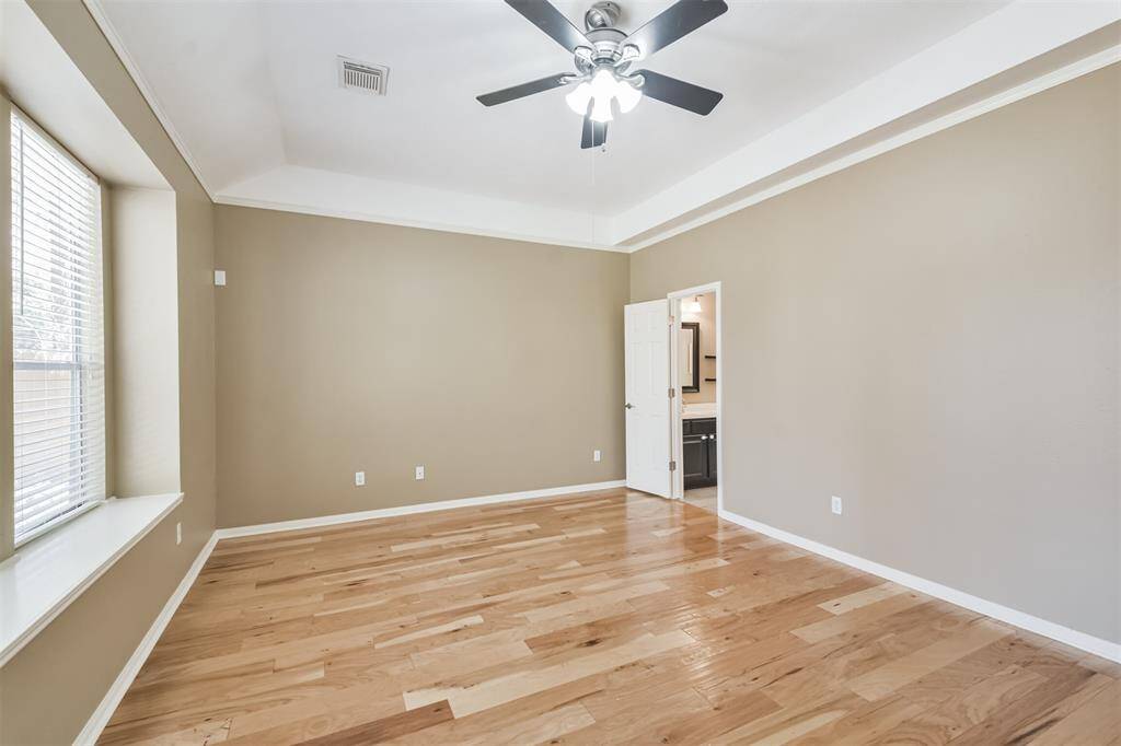 The spacious primary bedroom has the same wood flooring as main living areas and a ceiling fan.