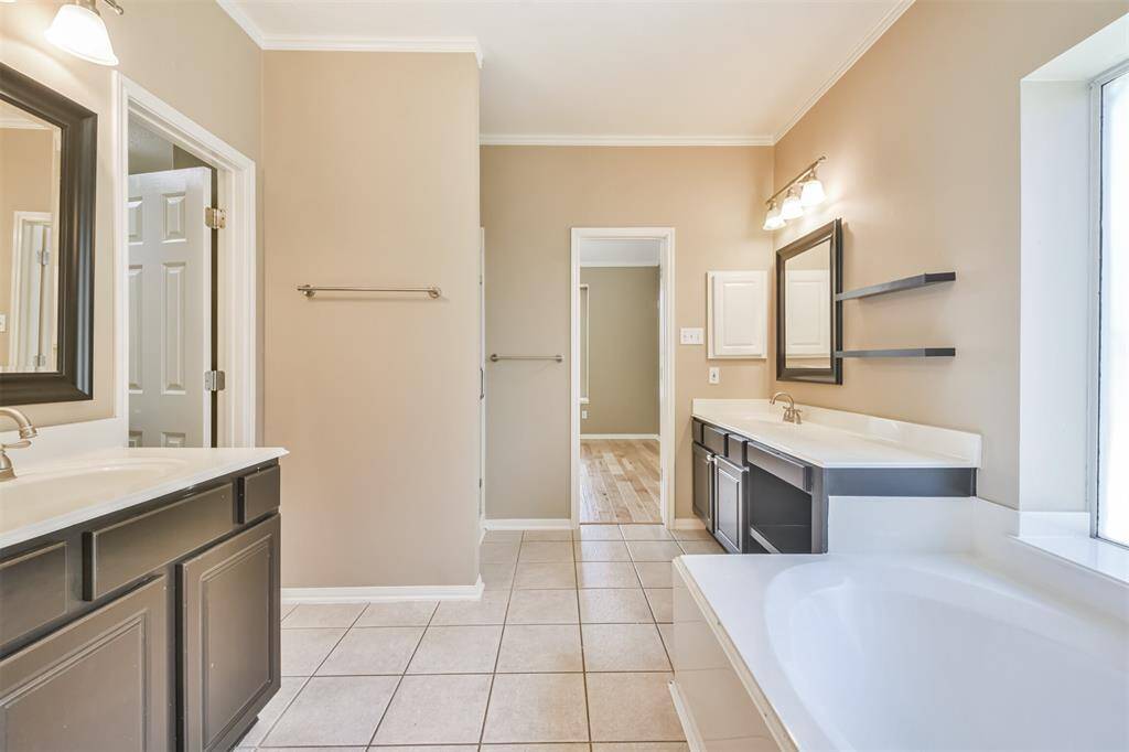 The primary bathroom features double vanities, a soaking tub, wood framed mirrors and extra shelving.
