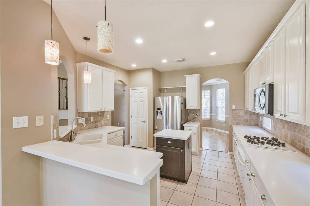 The kitchen is full of natural light and features solid surface counters, white cabinetry and a breakfast bar.