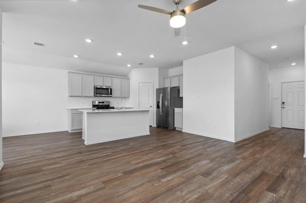 The open floor plan seamlessly connects the living, dining, and kitchen areas, featuring wood-like vinyl plank flooring, recessed lighting, and a ceiling fan for added comfort.