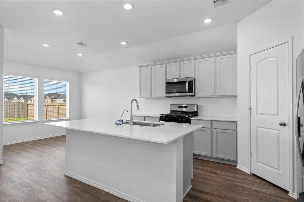 This stunning kitchen boasts sleek shaker cabinets, quartz countertops, a spacious island with a deep sink, and stainless steel appliances—including a gas range and built-in microwave.