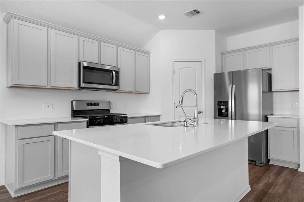 A chef’s dream! This modern kitchen features tall sleek shaker cabinets, quartz countertops, a large island with a deep sink, and stainless-steel appliances—including a gas range, built-in microwave, and side-by-side refrigerator.
