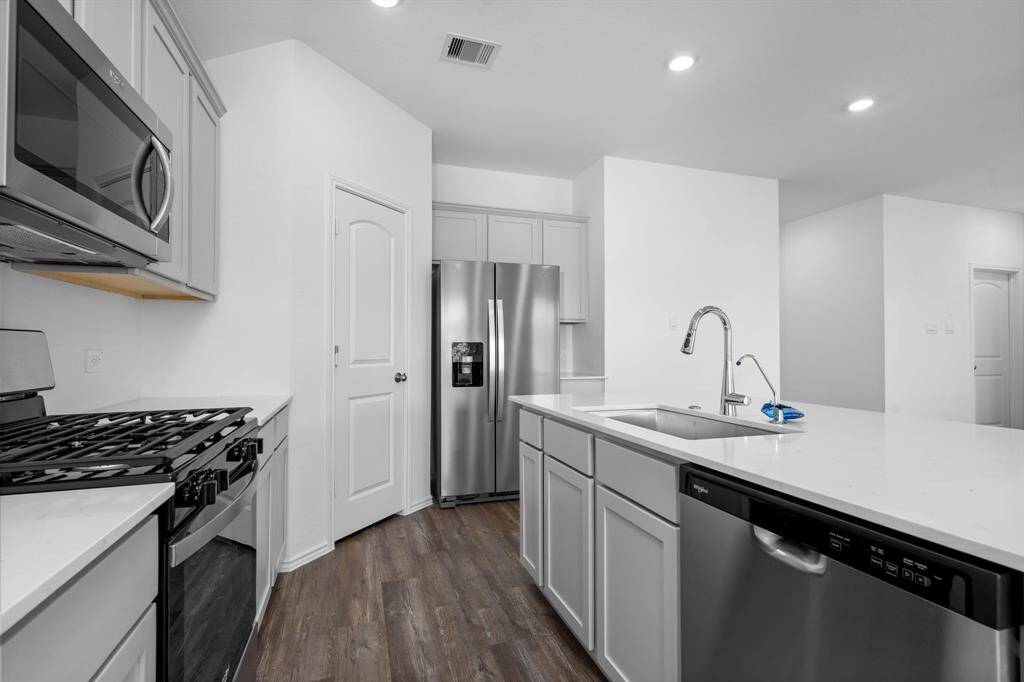 A sleek and functional kitchen boasting a freestanding gas range, built-in microwave, dishwasher, and a deep sink—all seamlessly integrated into the open floor plan.