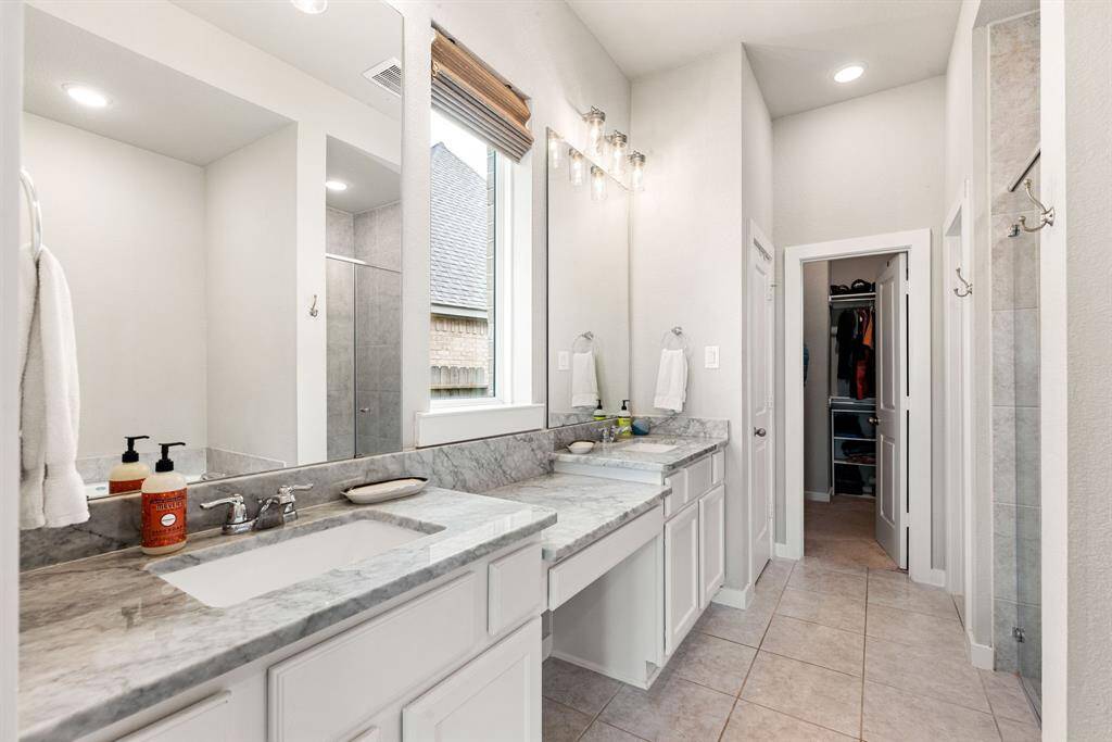 This primary bathroom is definitely move-in ready! Featuring a dark framed walk-in shower with tile surround, separate garden tub for soaking after a long day with custom tile detailing, dark stained cabinets with light countertops, spacious walk-in closet with shelving, high ceilings, custom paint, sleek and dark modern finishes.