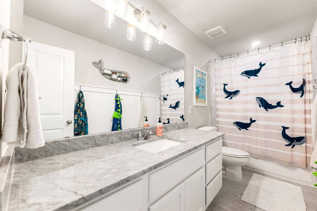 Secondary bathroom features light countertops and cabinets, custom paint, shower/tub combo with tile surround, large mirror, tile floors, sleek fixtures and modern finishes, plenty of space to accommodate any visiting family or guests.