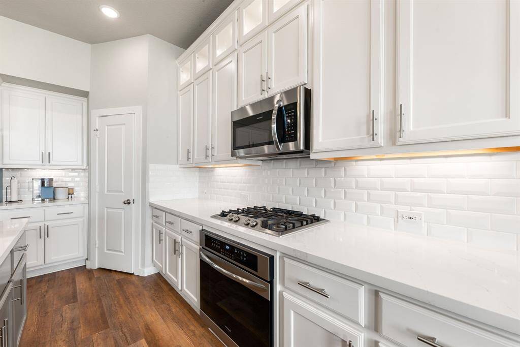 This stunning kitchen displays such a beautiful clean aesthetic with white cabinets, custom neutral paint, quartz countertops, light modern backsplash, and SS appliances, oversized kitchen island with extra storage, breakfast bar, recessed lighting, high ceilings and walk in pantry.